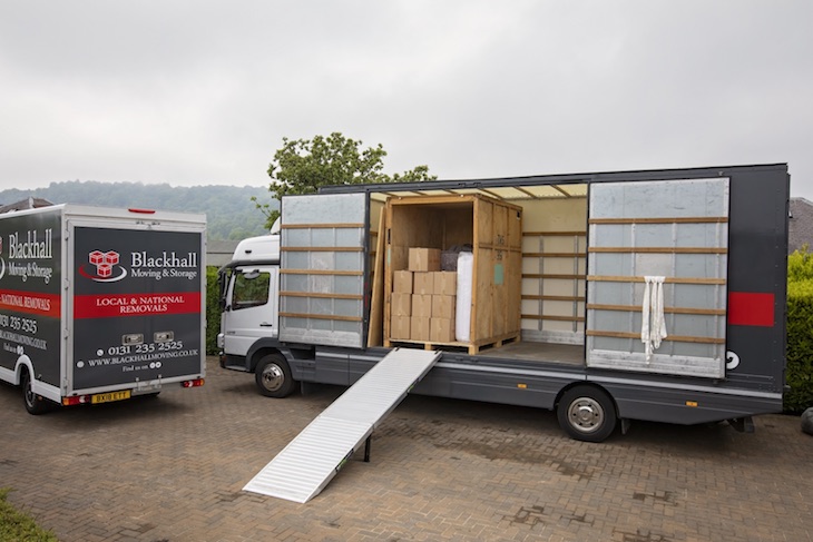 Two Blackhall removal vans, the larger van is being loaded from the side using a ramp