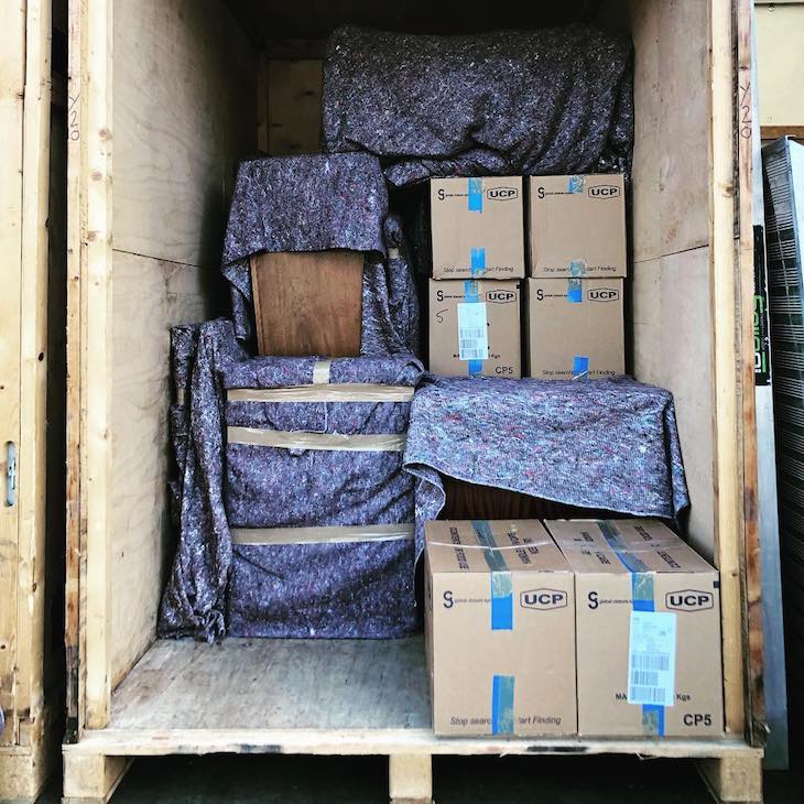 furniture wrapped in removal blankets, stacked with boxes inside storage container